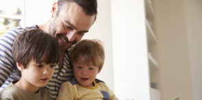 Close Up Of Father And Sons Reading Story At Home