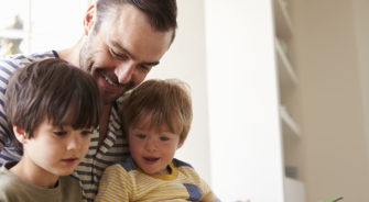 Close Up Of Father And Sons Reading Story At Home