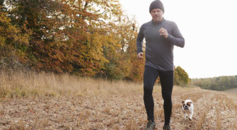 Mature Man Running Around Autumn Field With Pet Bulldog