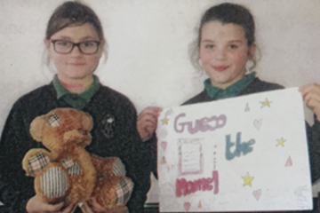 Two girls holding a teddy bear and a sign
