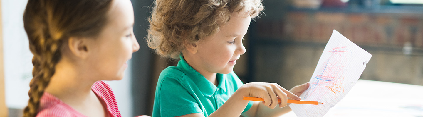 A boy drawing while his sister watches