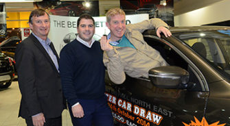 Three men at a car draw in a dealership