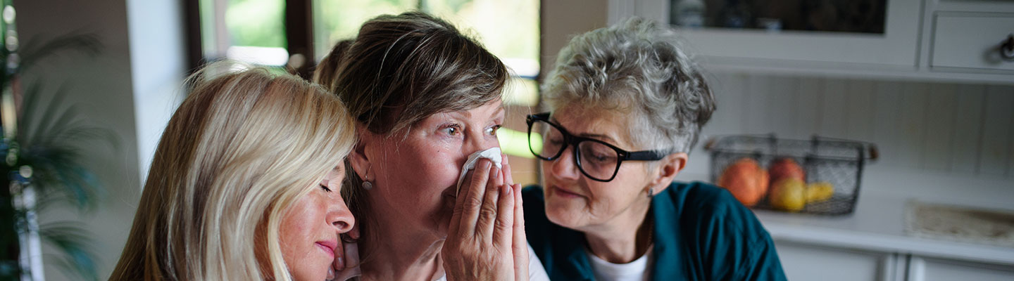 How we can help you. A lady fighting back tears as she receives help from two caring visitors.