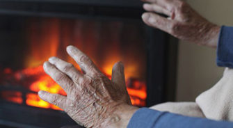 Old man heating his hands from a fireplace