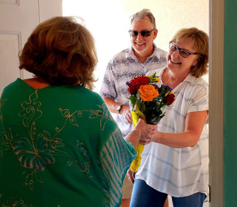 A woman takes away a bouquet of flowers from a couple outside their house