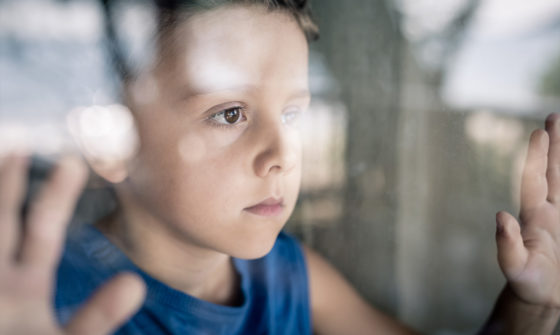 A sad boy leaning against the window