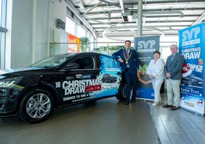 Three people standing next to a black ford focus which is for raffle