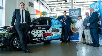 Three people standing next to a car up for raffle