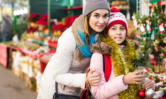 happy european woman with daughter looking at floral decoration at Cristmas fair